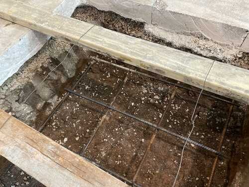 Rock and drainage work opened beside a property near a concrete driveway.